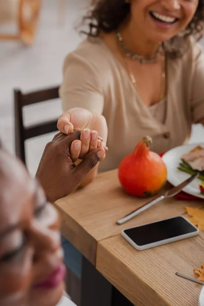 Vista recortada de la mujer afroamericana cogida de la mano con mamá borrosa mientras rezaba en la cena de acción de gracias - foto de stock