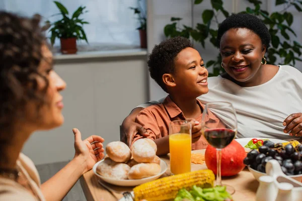 Heureuse femme afro-américaine étreignant petit-fils près de la table servie et fille floue pendant le dîner festif — Photo de stock
