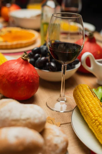 Glas Rotwein in der Nähe des ganzen Kürbisses, gegrilltes Mais und frische Trauben auf dem Tisch serviert mit Erntedankfest — Stockfoto