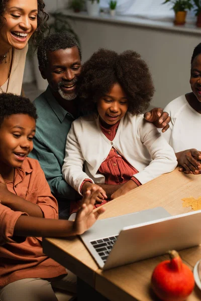 Афроамериканський хлопчик махає рукою біля ноутбука і усміхається сім'ї під час відеодзвінка в день подяки — стокове фото