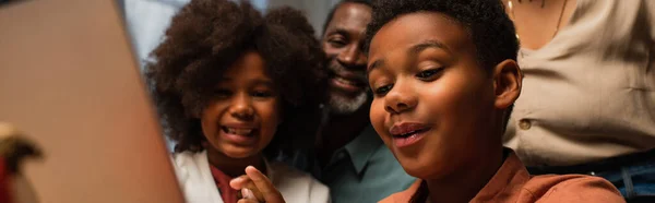 Схвильовані афроамериканські діти біля розмитого ноутбука під час відеодзвінка в день подяки, банер — стокове фото