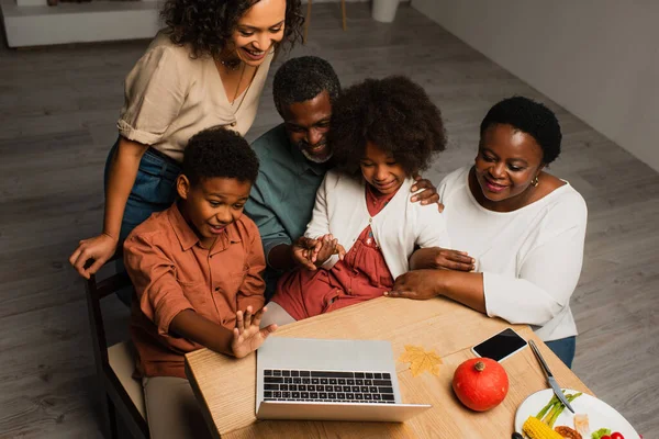 Happy african american boy waving hand near family during video call on laptop — Stock Photo