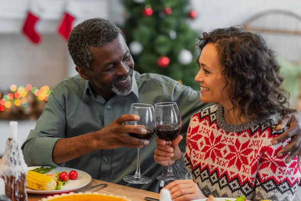 Joyful african american father and daughter clinking glasses of red wine during christmas dinner — Stock Photo