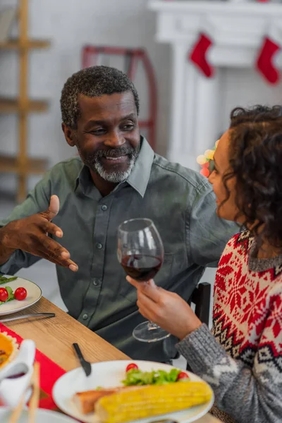 Mulher americana africana com copo de vinho tinto perto do pai falando durante o jantar de ação de graças — Fotografia de Stock