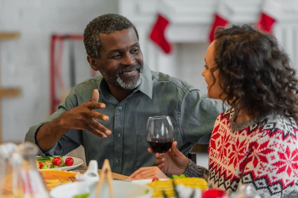 Uomo afro-americano sorridente gesticolare mentre parla con la figlia durante la cena di Natale — Foto stock