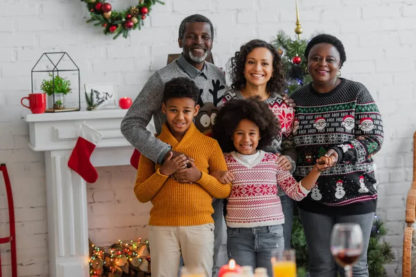 Fröhliche afrikanisch-amerikanische Familie hält Händchen und blickt in die Kamera am Kamin mit Weihnachtsdekoration — Stockfoto