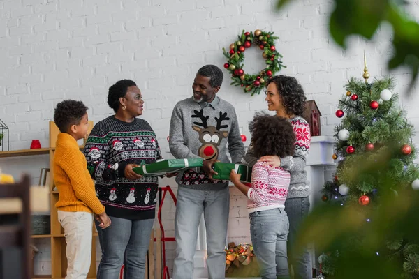 Bambini africani americani che presentano regali di Natale ai nonni compiaciuti vicino alla madre — Foto stock