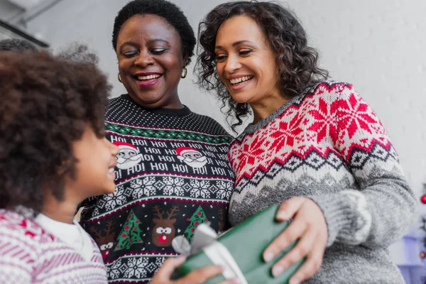 Low-Winkelaufnahme glücklicher afrikanisch-amerikanischer Frauen, die verschwommenen Mädchen ein Weihnachtsgeschenk machen — Stockfoto