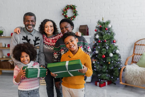 Crianças americanas africanas alegres com presentes de Natal olhando para a câmera perto de mãe e avós — Fotografia de Stock