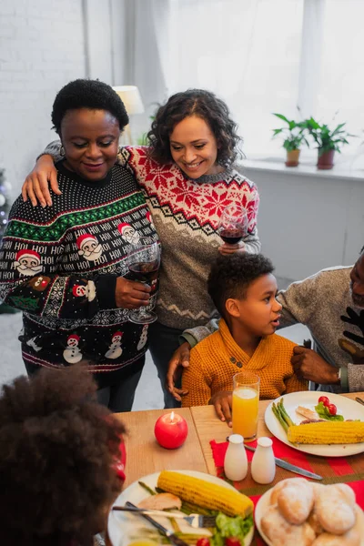 Feliz mulher afro-americana abraçando a mãe durante o jantar de Natal com a família — Fotografia de Stock