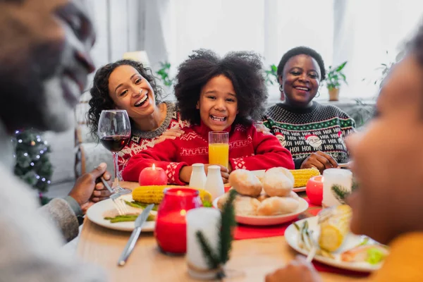 Allegre donne africane americane e ragazza ridere vicino ragazzo offuscata e nonno durante la cena di Natale — Foto stock