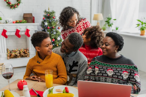 Glückliche afrikanisch-amerikanische Familie in der Nähe von Laptop auf dem Tisch serviert mit festlichem Abendessen — Stockfoto