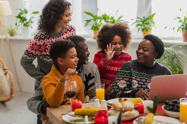 Alegre afroamericano chica saludando mano durante videollamada cerca de familia - foto de stock