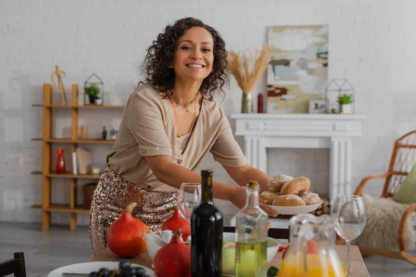 Felice donna afro-americana che tiene panini fatti in casa vicino al tavolo servito con la cena del Ringraziamento — Foto stock