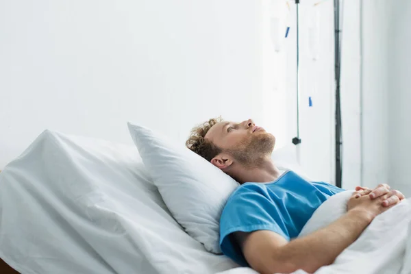 Lockiger junger Patient mit geballten Händen auf dem Krankenhausbett liegend — Stockfoto