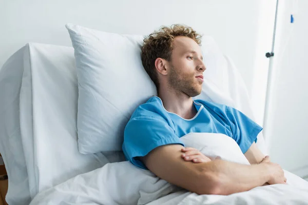 Curly young patient with crossed arms in hospital bed — Stock Photo