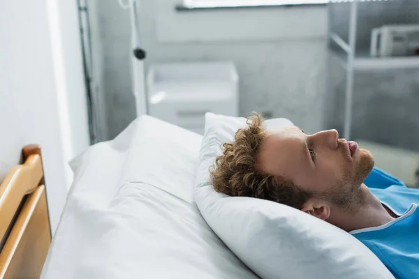 Encaracolado jovem paciente olhando para cima enquanto deitado na cama do hospital — Fotografia de Stock