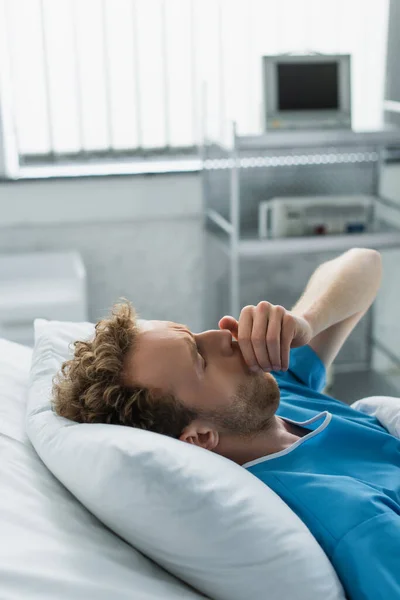 Paciente enfermo tosiendo mientras está acostado en la cama del hospital - foto de stock