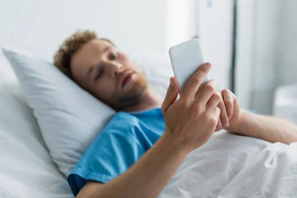 Blurred patient using smartphone while lying in hospital bed — Stock Photo