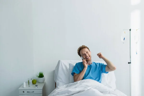 Bouclé homme en robe de patient parler sur smartphone à l'hôpital — Photo de stock