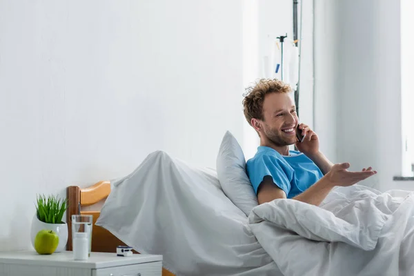 Fröhlicher Mann, der im Krankenhaus gestikuliert und auf dem Smartphone spricht — Stockfoto