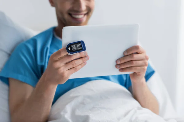 Ausgeschnittene Ansicht einer glücklichen Patientin mit Oximeter am Finger mit digitalem Tablet im Krankenhaus — Stockfoto