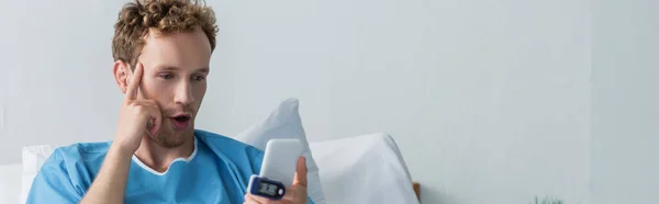 Surprised patient with oximeter on finger using smartphone in hospital, banner — Stock Photo