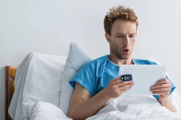 Patientin mit Oximeter am Finger mit digitalem Tablet im Krankenhaus überrascht — Stockfoto