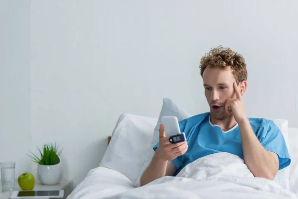 Paciente sorprendido con oxímetro en el dedo usando teléfono inteligente en el hospital - foto de stock