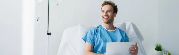Freelancer feliz em vestido de paciente usando laptop na cama do hospital, banner — Fotografia de Stock