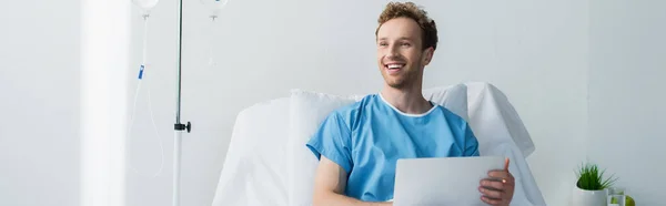 Freelancer feliz em vestido de paciente usando laptop na cama do hospital, banner — Fotografia de Stock