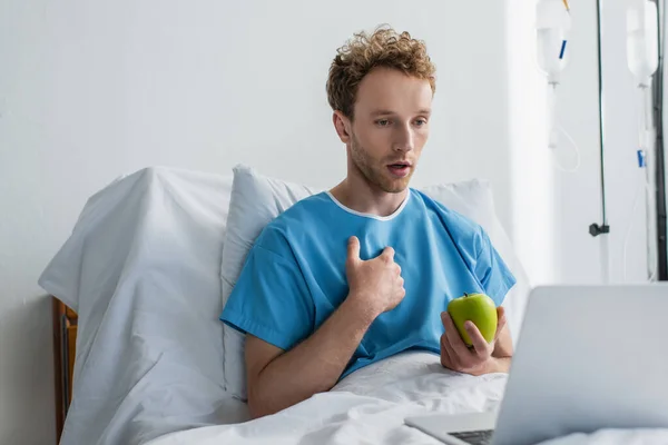Хворий чоловік має відеодзвінок, тримаючи яблуко в лікарні — стокове фото