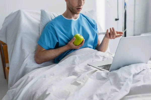Corte vista de doente homem ter vídeo chamada enquanto segurando maçã no hospital — Fotografia de Stock