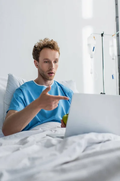 Kranker Mann mit Videoanruf während er gestikuliert und Apfel im Krankenhaus hält — Stockfoto