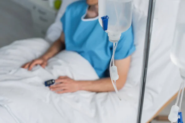 Contador de gota com frasco de terapia intravenosa perto do paciente desfocado na cama do hospital — Fotografia de Stock