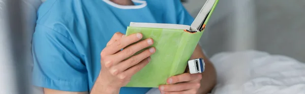 Partial view of patient with oximeter on finger reading book in hospital, banner — Stock Photo