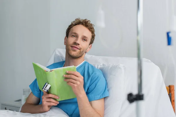 Pleased patient with oximeter on finger holding book in hospital — Stock Photo