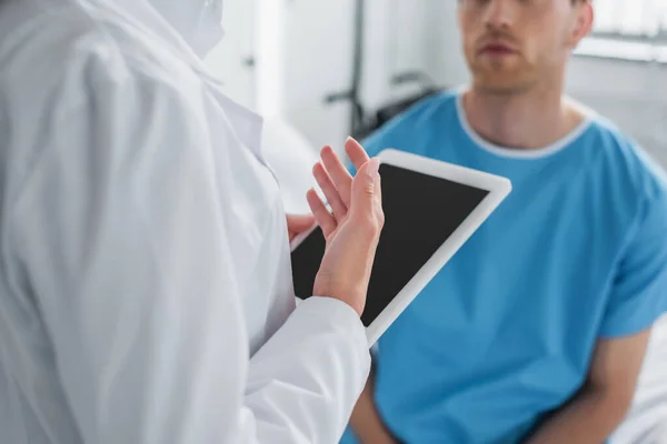 Обрезанный вид врача в белом халате с цифровой таблеткой рядом с пациентом — стоковое фото