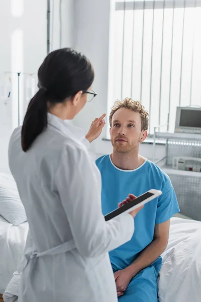Doctor in white coat holding digital tablet and pointing at curly patient — Stock Photo