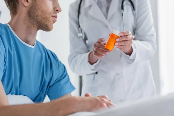 Vista recortada del médico en una botella de abrigo blanco con medicamentos cerca del paciente - foto de stock