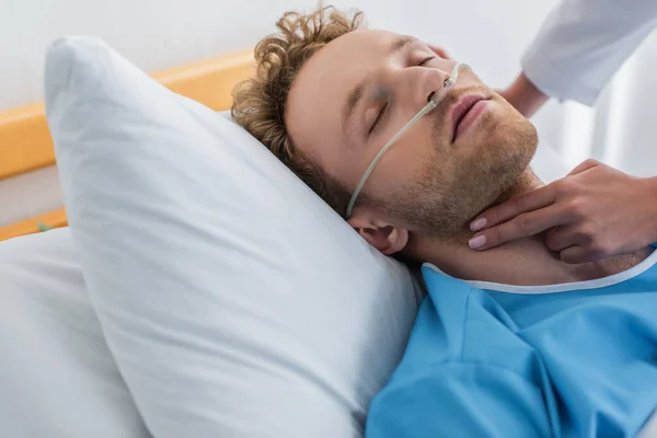 Doctor checking pulse of curly patient with nasal cannula — Stock Photo