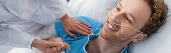 Hochwinkelaufnahme des Arztes, der lächelnde Patienten mit Nasenkanüle an der Hand hält, Banner — Stockfoto