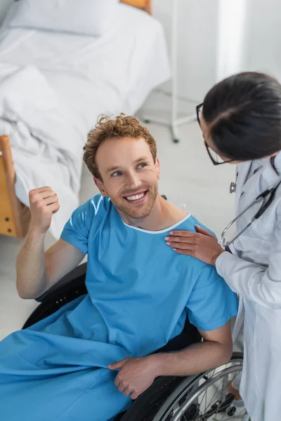 Blick aus der Vogelperspektive auf einen Arzt im weißen Kittel in der Nähe eines fröhlichen behinderten Patienten im Rollstuhl — Stockfoto