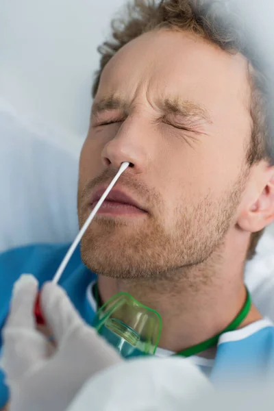 Médico sosteniendo hisopo cerca de la nariz del paciente con los ojos cerrados mientras hace la prueba de pcr - foto de stock