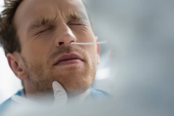 Médico en guante de látex sosteniendo hisopo cerca de la nariz del paciente con los ojos cerrados mientras hace la prueba de pcr — Stock Photo