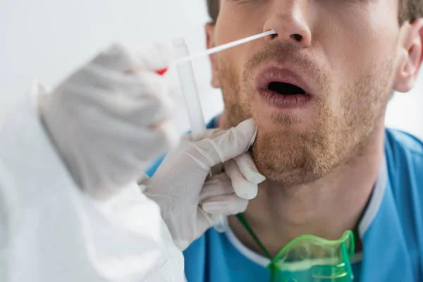 Vista recortada del médico en guantes de látex sosteniendo hisopo cerca de la nariz del paciente mientras se hace la prueba de pcr nasal - foto de stock