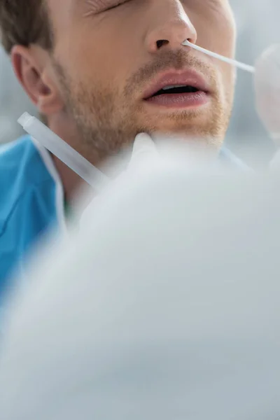 Cropped view of doctor holding swab near nose of patient while doing nasal pcr test in clinic — Stock Photo