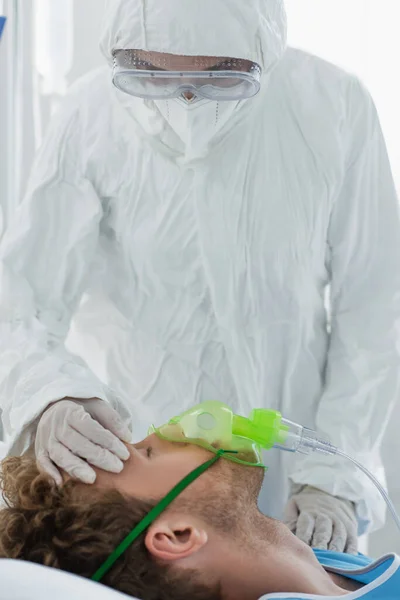 Médico en equipo de protección personal que examina al paciente con máscara de oxígeno - foto de stock
