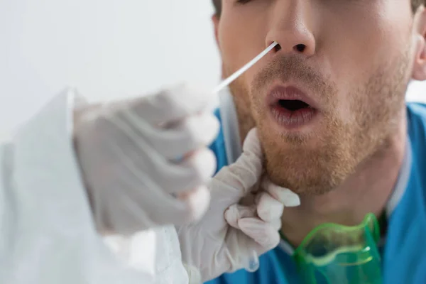 Partial view of doctor in latex gloves holding swab near nose of curly patient while doing nasal pcr test — Stock Photo