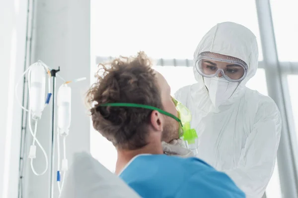 Médecin en équipement de protection individuelle et lunettes examinant le patient en masque à oxygène à l'hôpital — Photo de stock